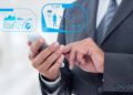 A person in a suit using a smartphone to display holographic scientific and data icons. | FintechZoom