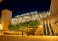 The entrance to the Dubai Exhibition Centre at night, featuring a lit sign, outdoor escalators, and stairs. | FintechZoom