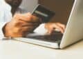 A person holding a bank card while typing on a laptop. | FintechZoom