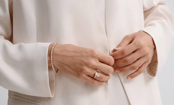 A person wearing a gold tennis bracelet and a gold ring with a single oval-cut stone. | FintechZoom